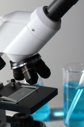 Photo of Microscope with glass slide and glassware in laboratory, closeup