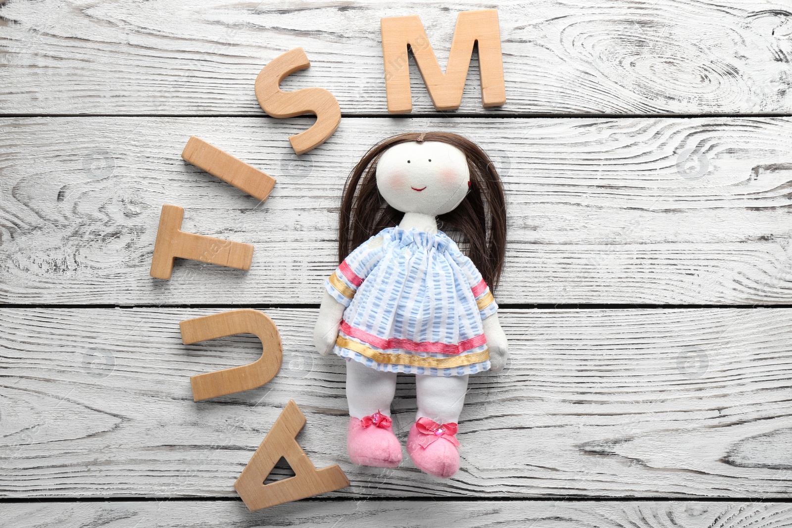 Photo of Word "Autism" and doll on wooden background, flat lay