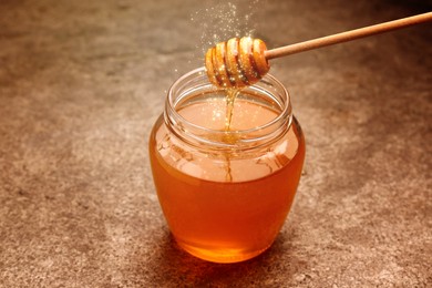 Natural honey dripping from dipper into glass jar on table under sunlight