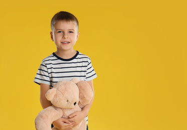 Photo of Little boy with toy bear on yellow background. Space for text