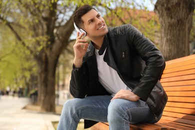 Handsome man with headphones listening to music while sitting on bench in park