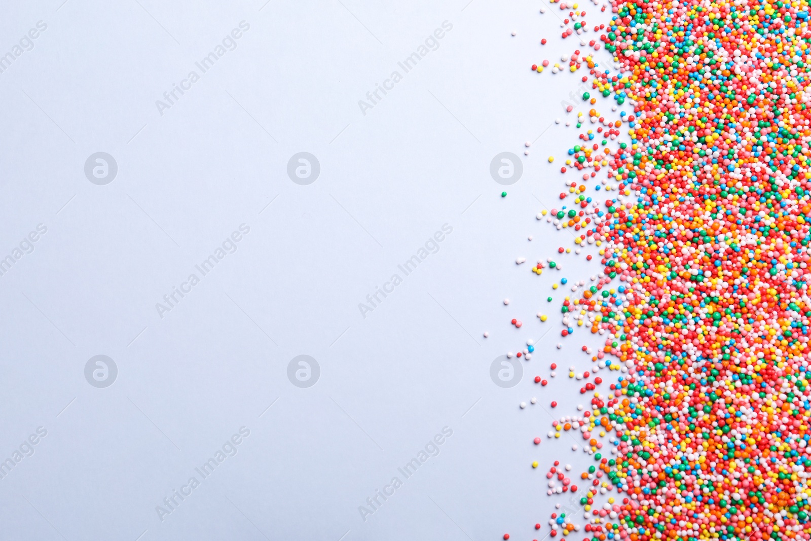 Photo of Colorful sprinkles on light grey background, flat lay with space for text. Confectionery decor