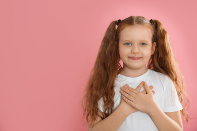 Cute grateful little girl with hands on chest against pink background. Space for text