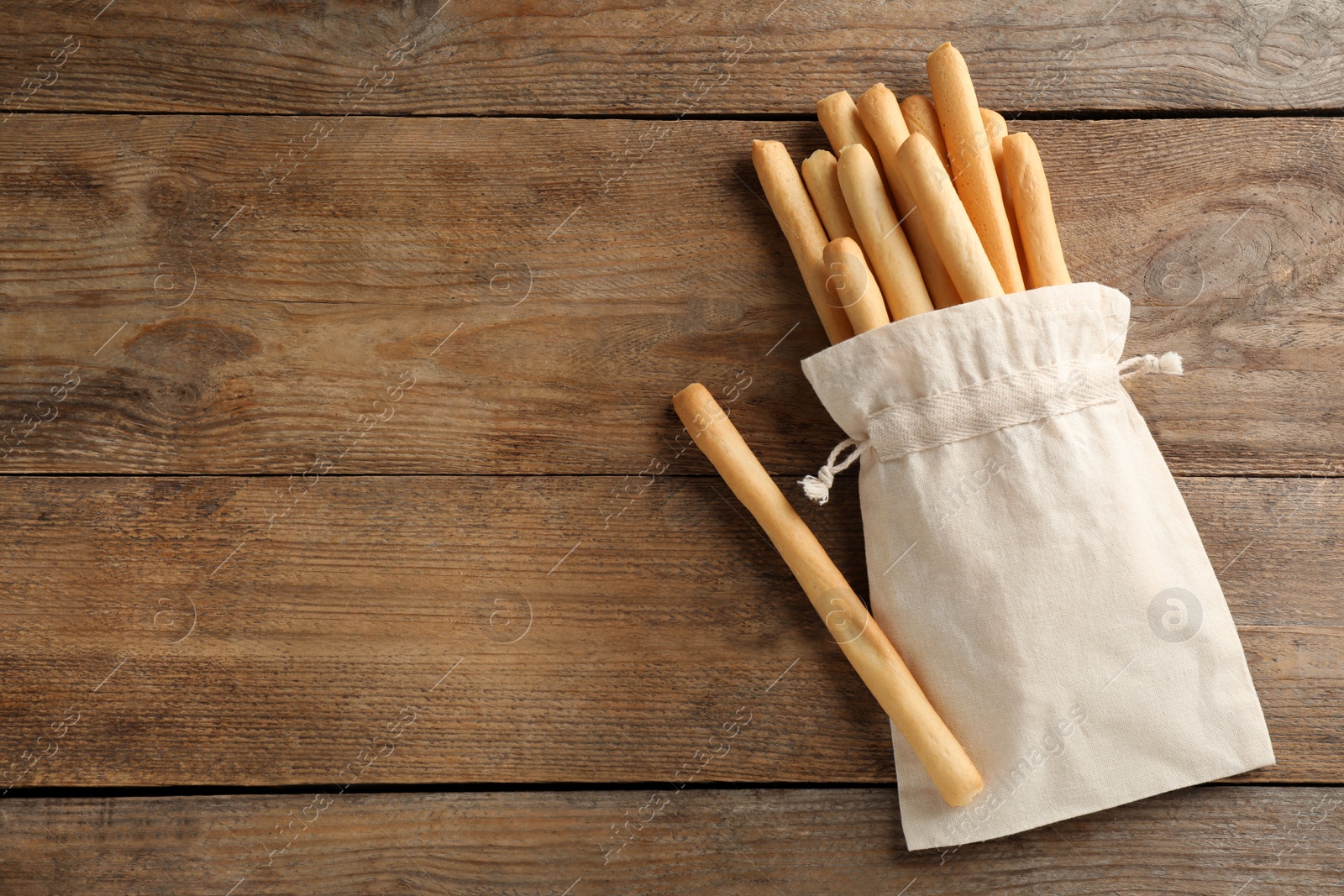 Photo of Delicious grissini sticks in bag on wooden table, flat lay. Space for text