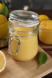 Photo of Delicious lemon curd in glass jar, fresh citrus fruit and green leaf on table