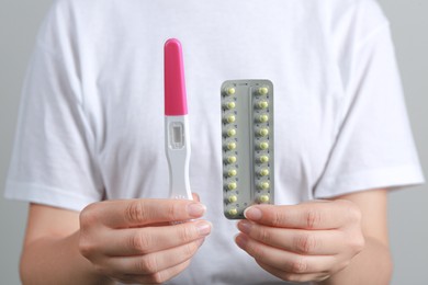 Photo of Woman holding birth control pills pregnancy test on grey background, closeup