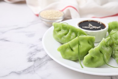 Photo of Delicious green dumplings (gyozas) and soy sauce on white marble table, closeup. Space for text