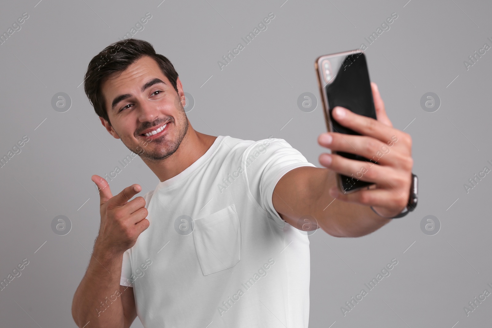 Photo of Handsome young man taking selfie with smartphone on grey background