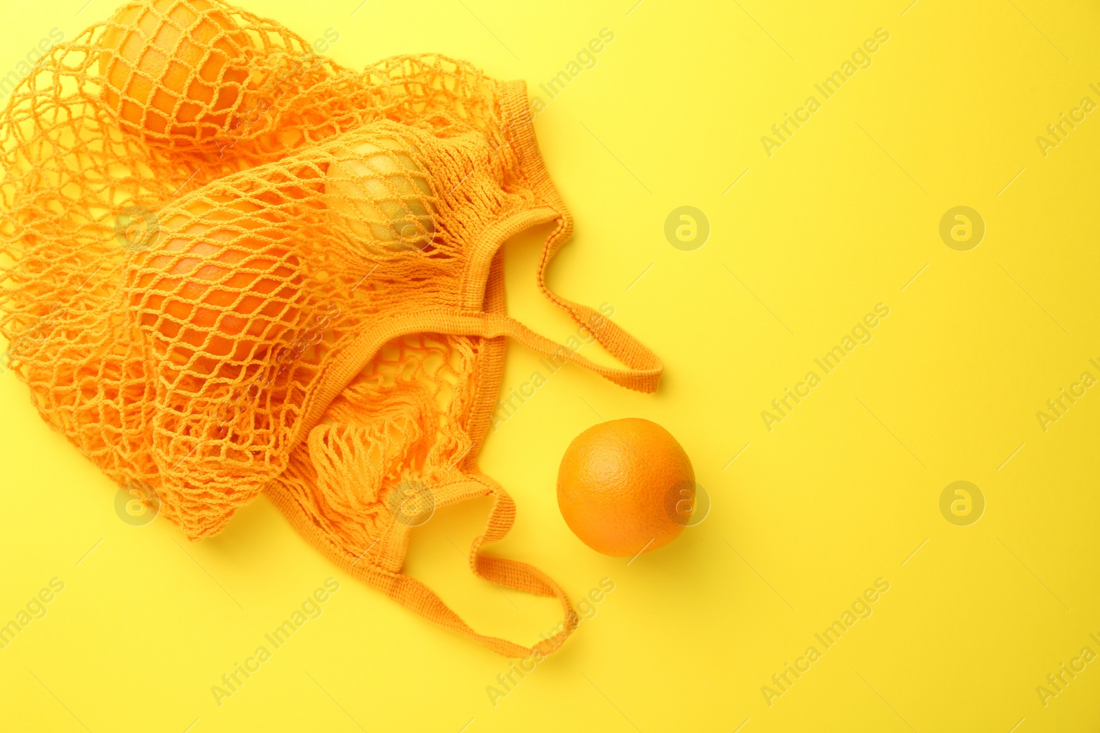 Photo of String bag with fresh oranges on yellow background, top view. Space for text