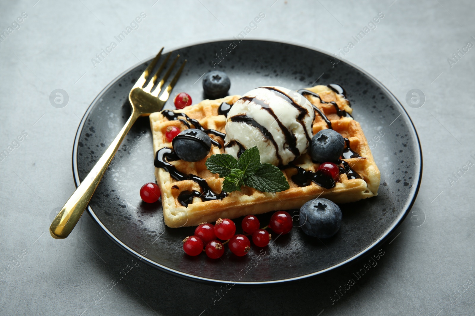 Photo of Delicious Belgian waffle with ice cream, berries and chocolate sauce on grey table