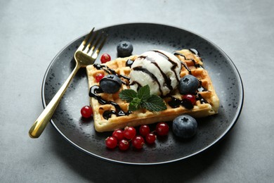 Delicious Belgian waffle with ice cream, berries and chocolate sauce on grey table