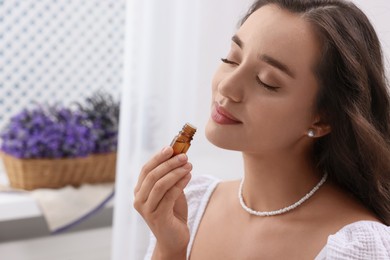 Photo of Beautiful young woman with bottle of essential oil indoors