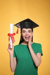 Emotional student with graduation hat and diploma on yellow background