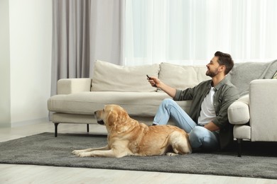 Photo of Man turning on TV near his cute Labrador Retriever at home