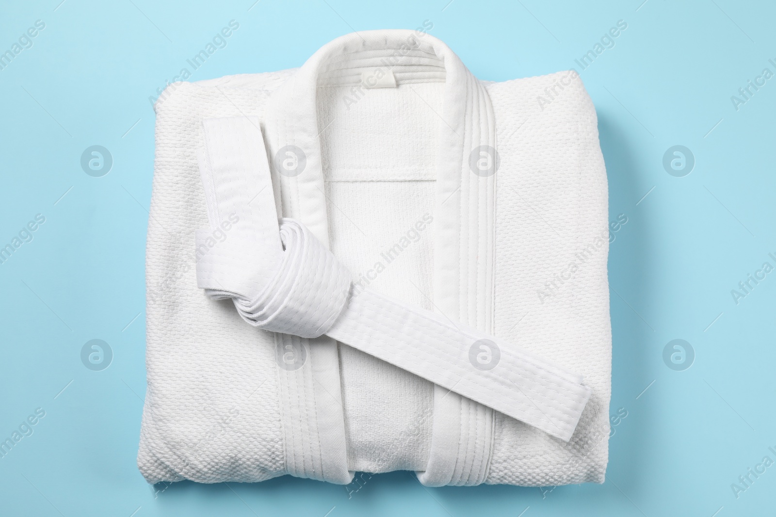 Photo of White karate belt and kimono on light blue background, top view