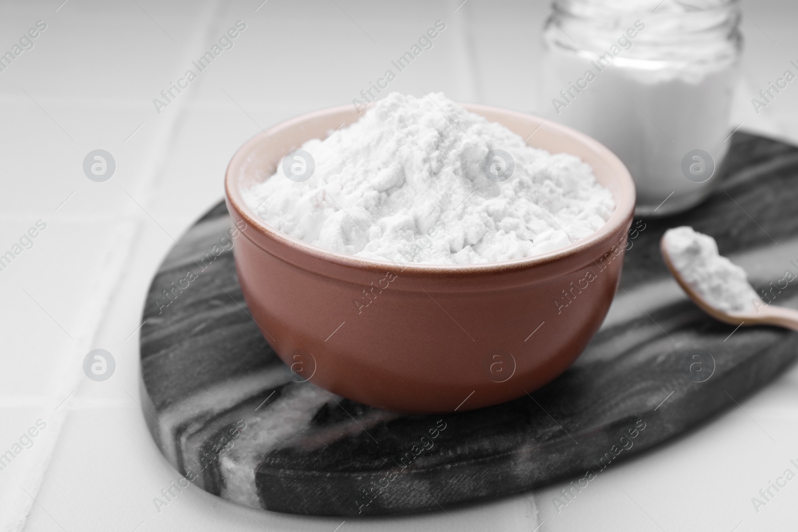 Photo of Bowl, spoon and glass jar of natural starch on white tiled table