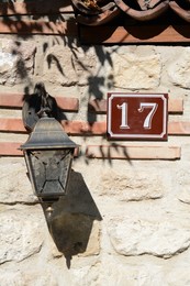 Photo of Plate with house number seventeen near lantern on stone wall outdoors