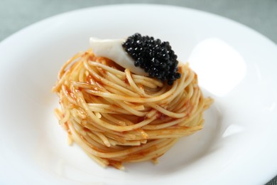 Tasty spaghetti with tomato sauce and black caviar on plate, closeup. Exquisite presentation of pasta dish