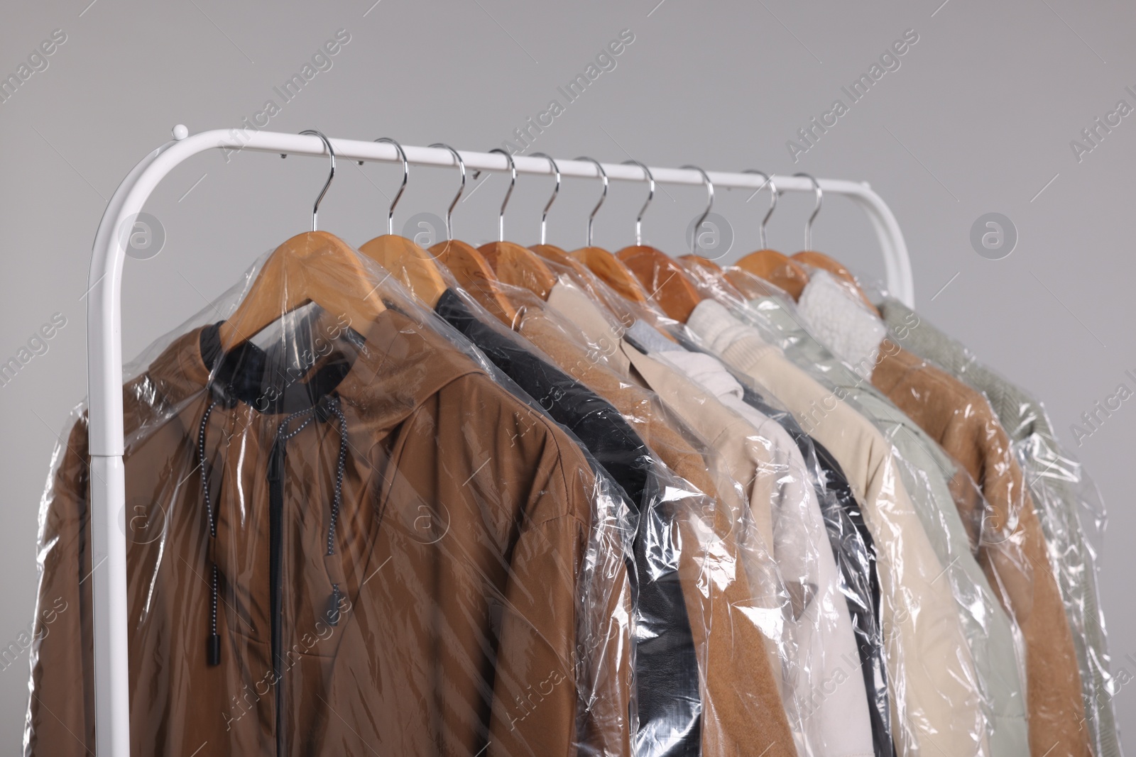 Photo of Dry-cleaning service. Many different clothes in plastic bags hanging on rack against grey background