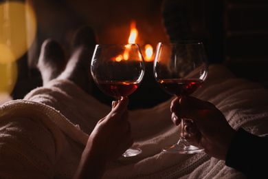 Couple with glasses of red wine near burning fireplace, closeup