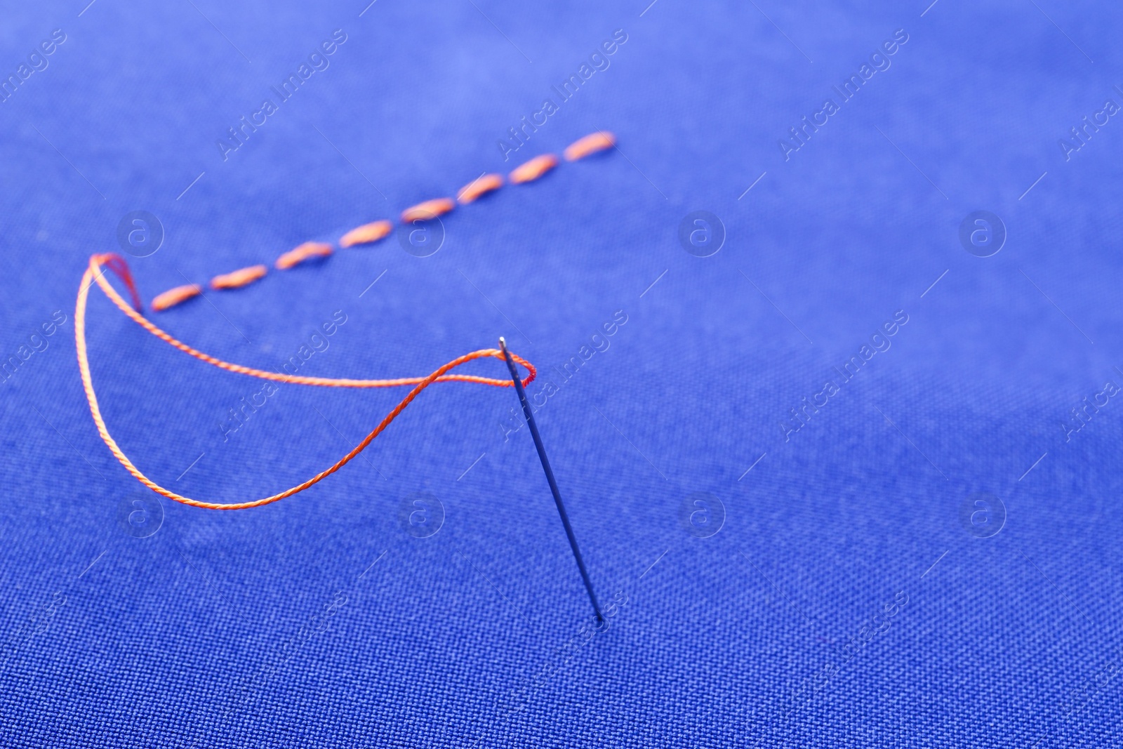 Photo of Sewing needle with thread and stitches on blue cloth, closeup
