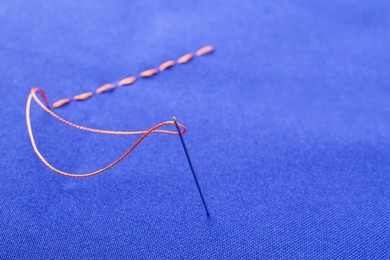 Photo of Sewing needle with thread and stitches on blue cloth, closeup