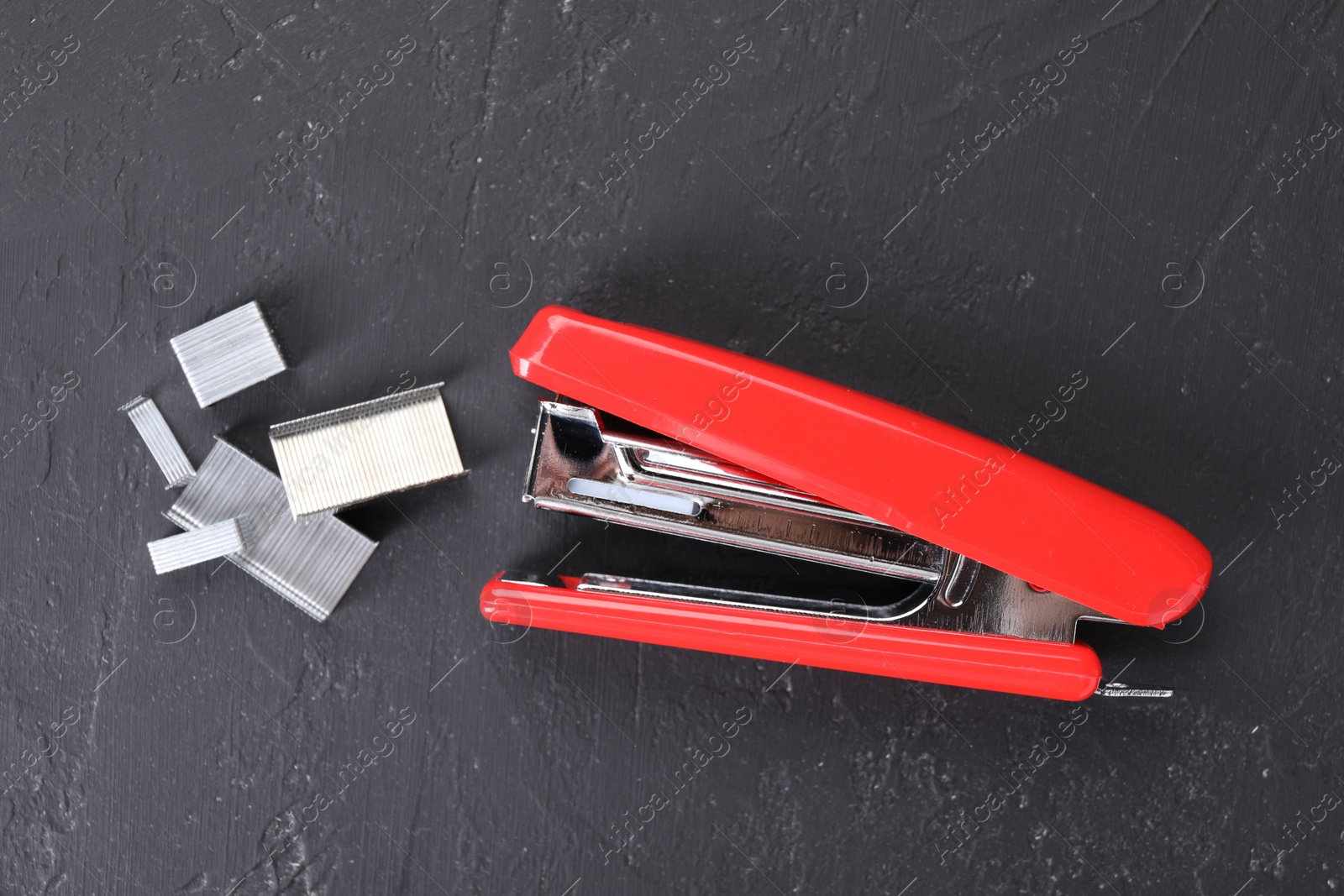 Photo of Red stapler with staples on black textured table, flat lay