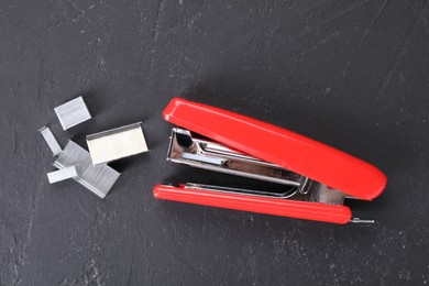 Red stapler with staples on black textured table, flat lay