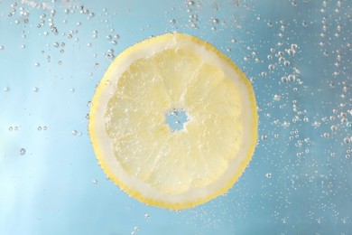 Photo of Juicy lemon slice in soda water against light blue background, closeup