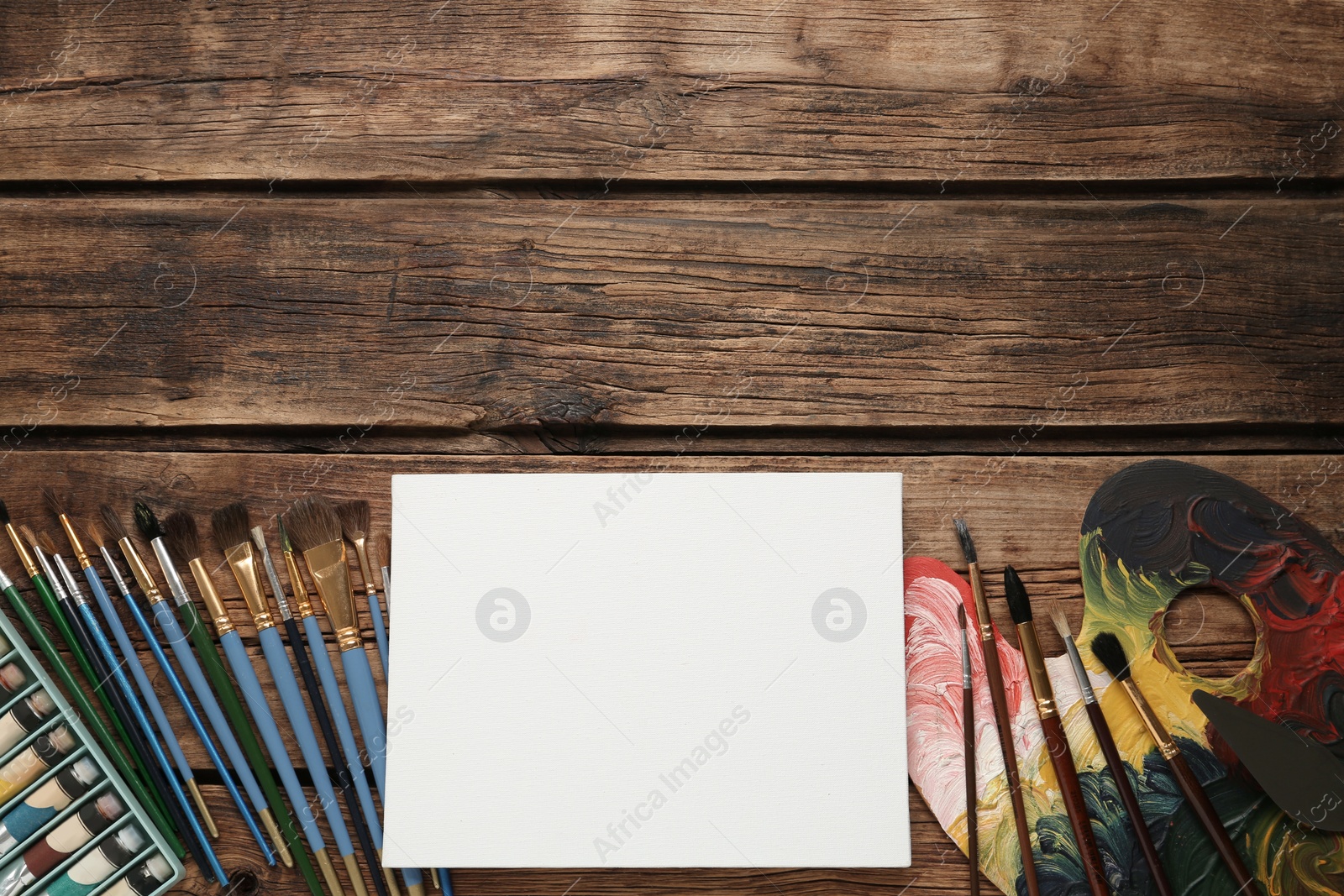 Photo of Blank canvas, brushes, palette and paints on wooden table, flat lay. Space for text