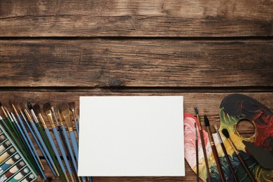 Photo of Blank canvas, brushes, palette and paints on wooden table, flat lay. Space for text