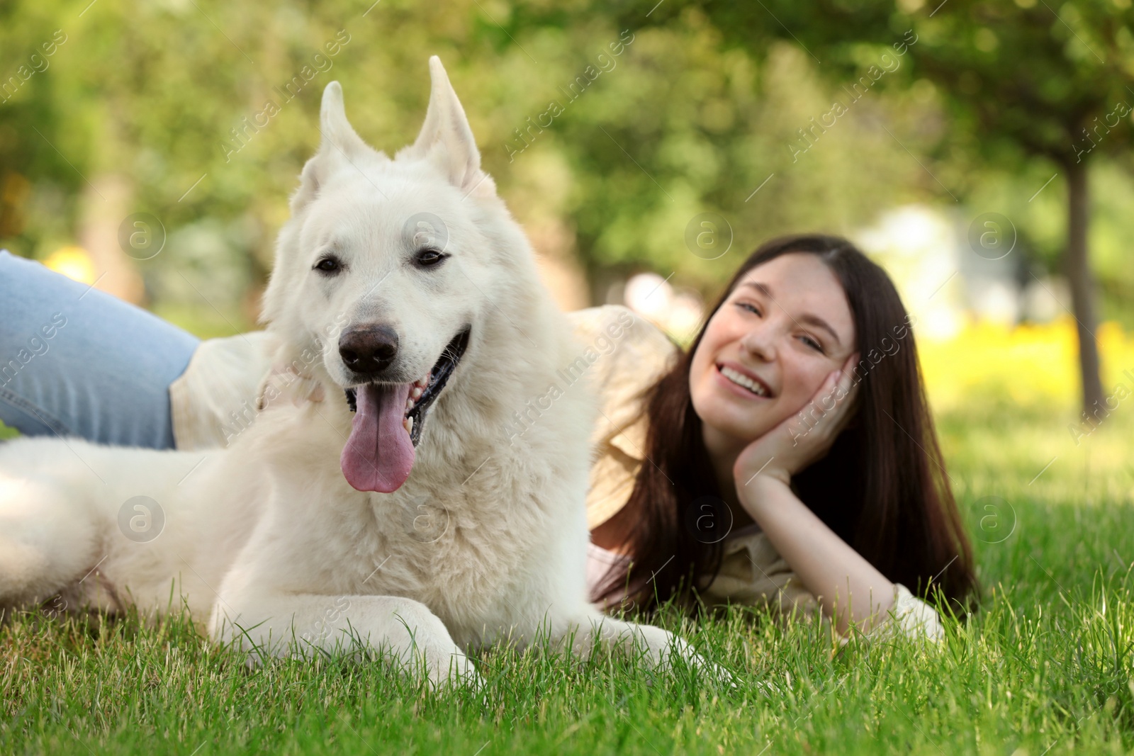 Photo of Teenage girl lying with her white Swiss Shepherd dog on green grass in park