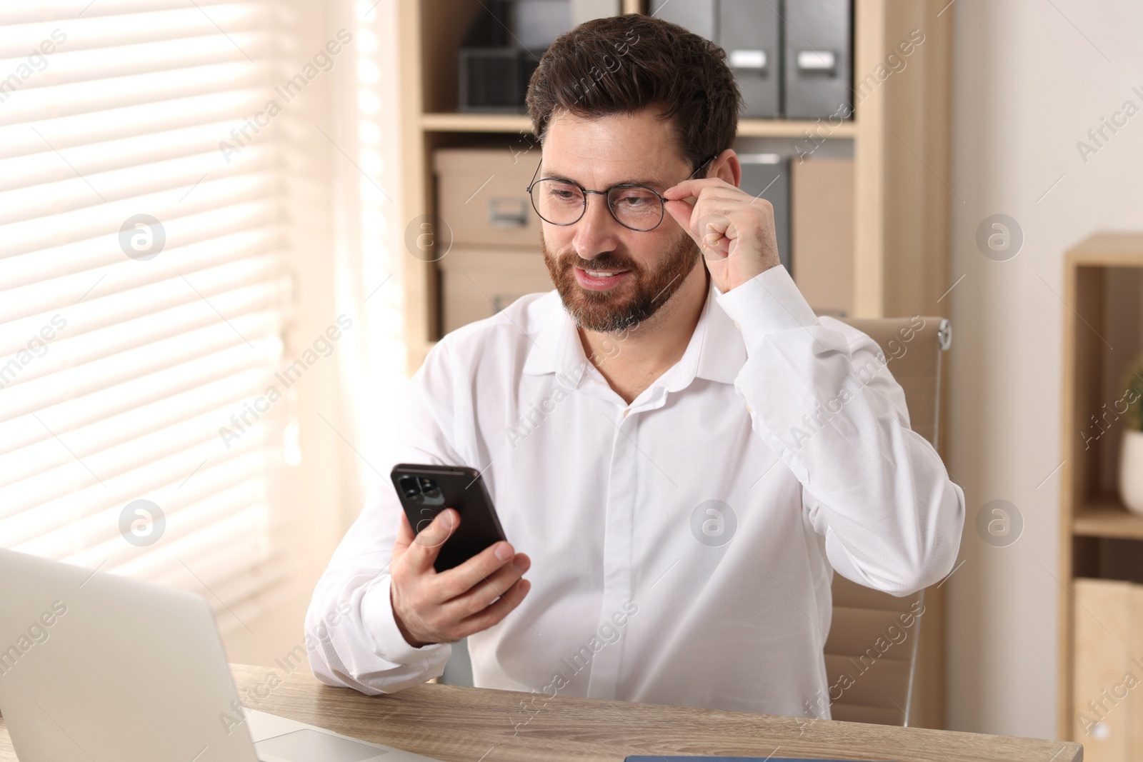 Photo of Smiling man using smartphone at table in office