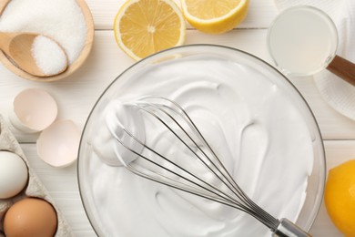 Bowl with whipped cream, whisk and ingredients on white wooden table, flat lay