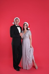 Photo of Beautiful happy couple in Christmas hats on red background