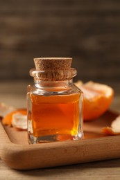Photo of Bottle of tangerine essential oil and peeled fresh fruit on wooden table