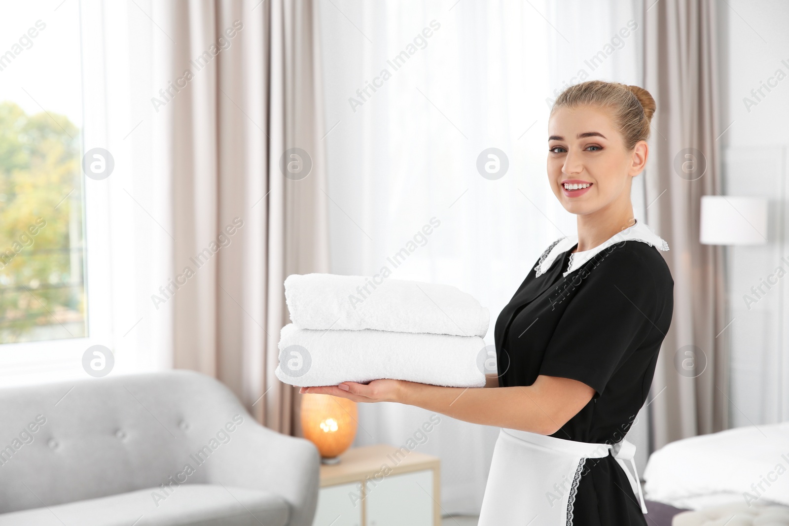 Photo of Young chambermaid with clean towels in hotel room. Space for text