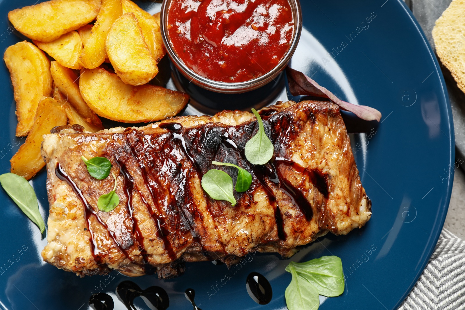 Photo of Delicious grilled ribs with potatoes and sauce on table, top view