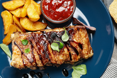 Photo of Delicious grilled ribs with potatoes and sauce on table, top view
