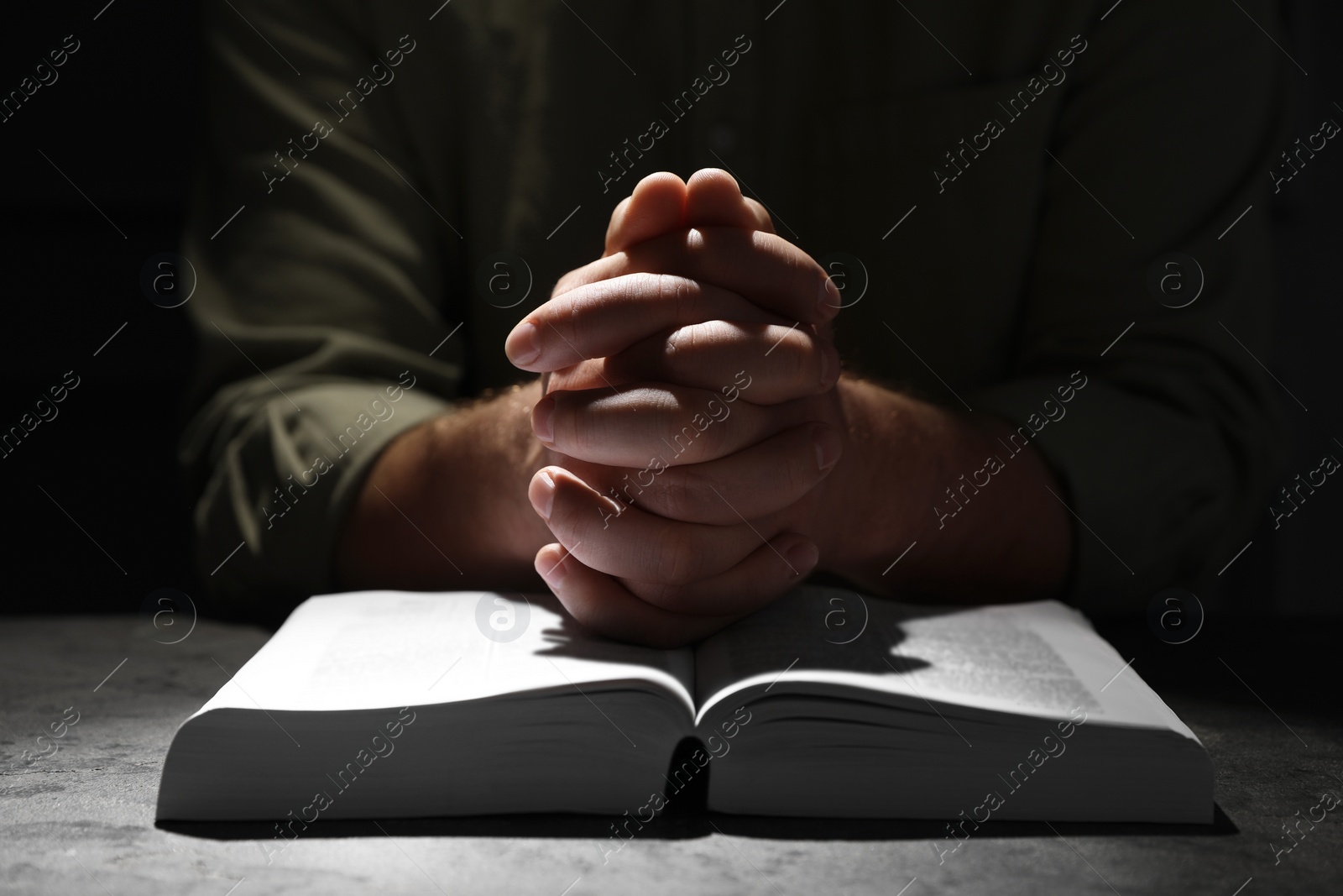 Photo of Religion. Christian man praying over Bible at table, closeup