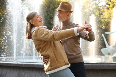 Photo of Affectionate senior couple dancing together near fountain outdoors