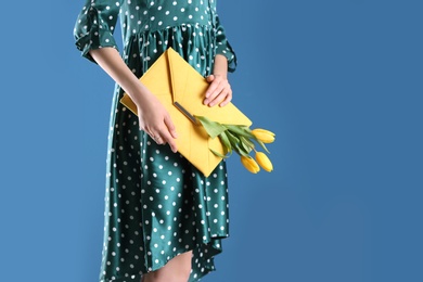 Woman holding elegant clutch with spring flowers on blue background, closeup. Space for text