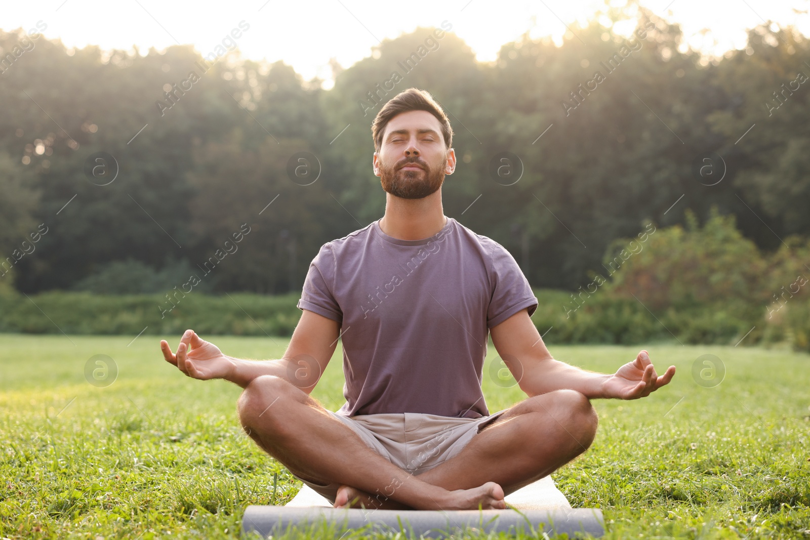 Photo of Man practicing yoga on mat outdoors. Lotus pose