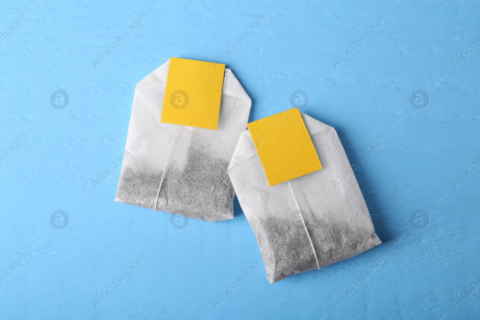 Photo of Tea bags with tabs on light blue wooden table, top view