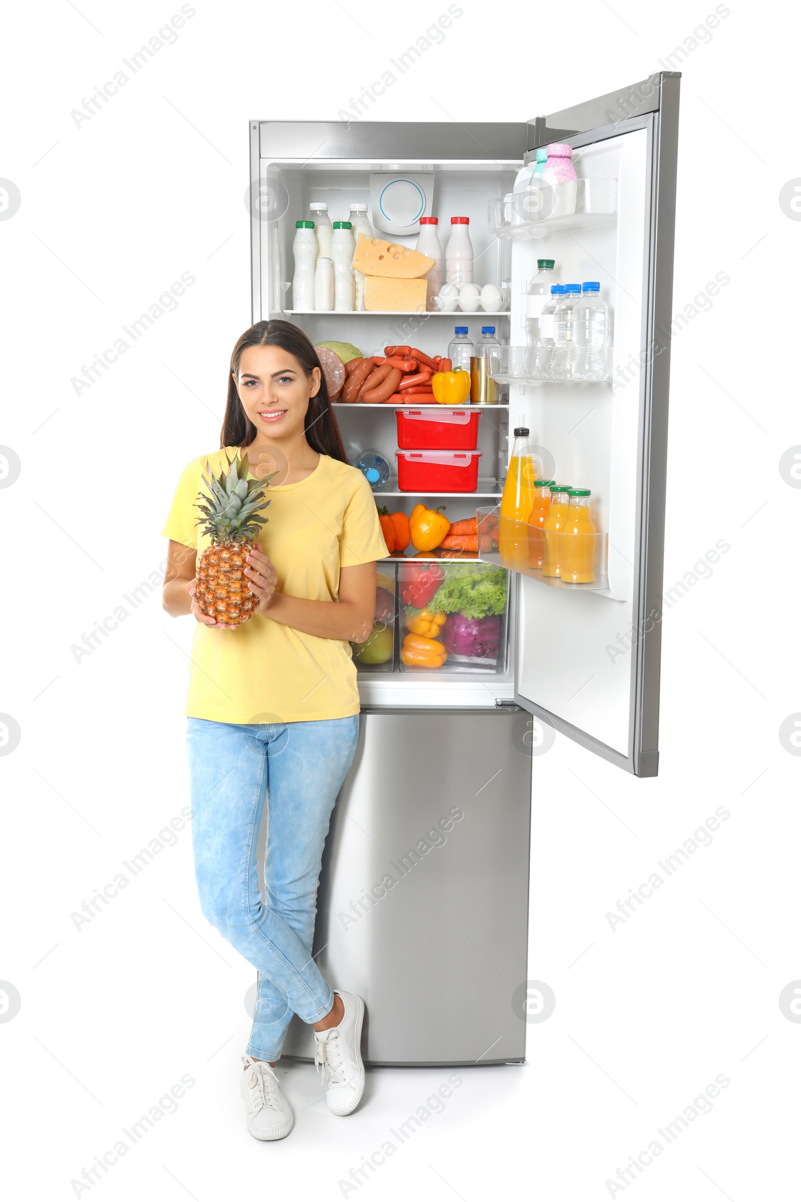 Photo of Young woman with pineapple near open refrigerator on white background