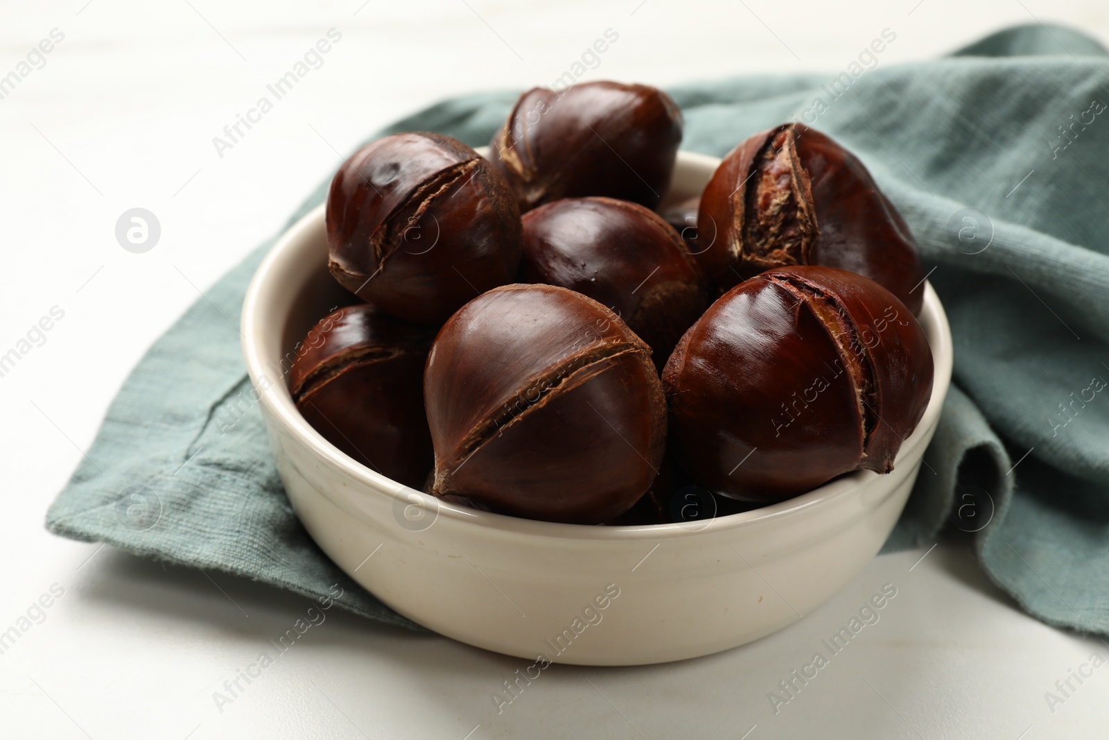 Photo of Roasted edible sweet chestnuts in bowl on white table, closeup