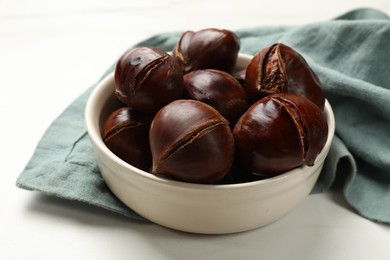 Photo of Roasted edible sweet chestnuts in bowl on white table, closeup