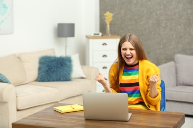 Happy young woman playing online lottery using laptop at home