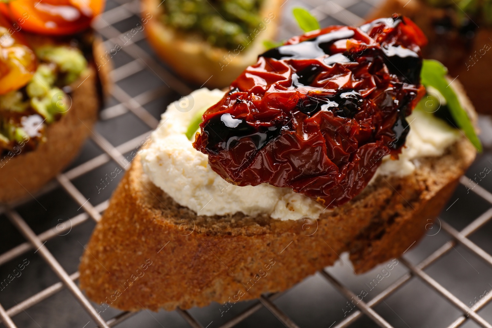 Photo of Delicious bruschetta with sun-dried tomatoes, cream cheese and balsamic vinegar on cooling rack, closeup