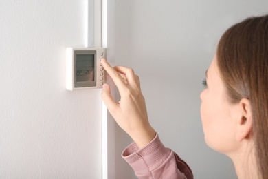 Woman adjusting thermostat on white wall. Heating system